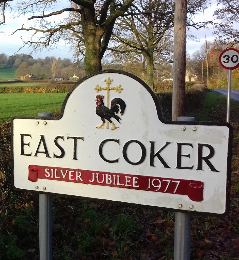 A road sign saying East Coker with fields behind
