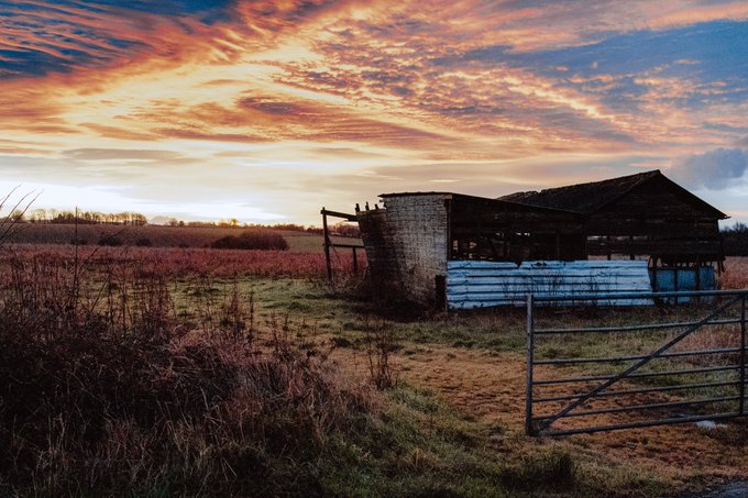 A run down barn set against a pink sky and fiels