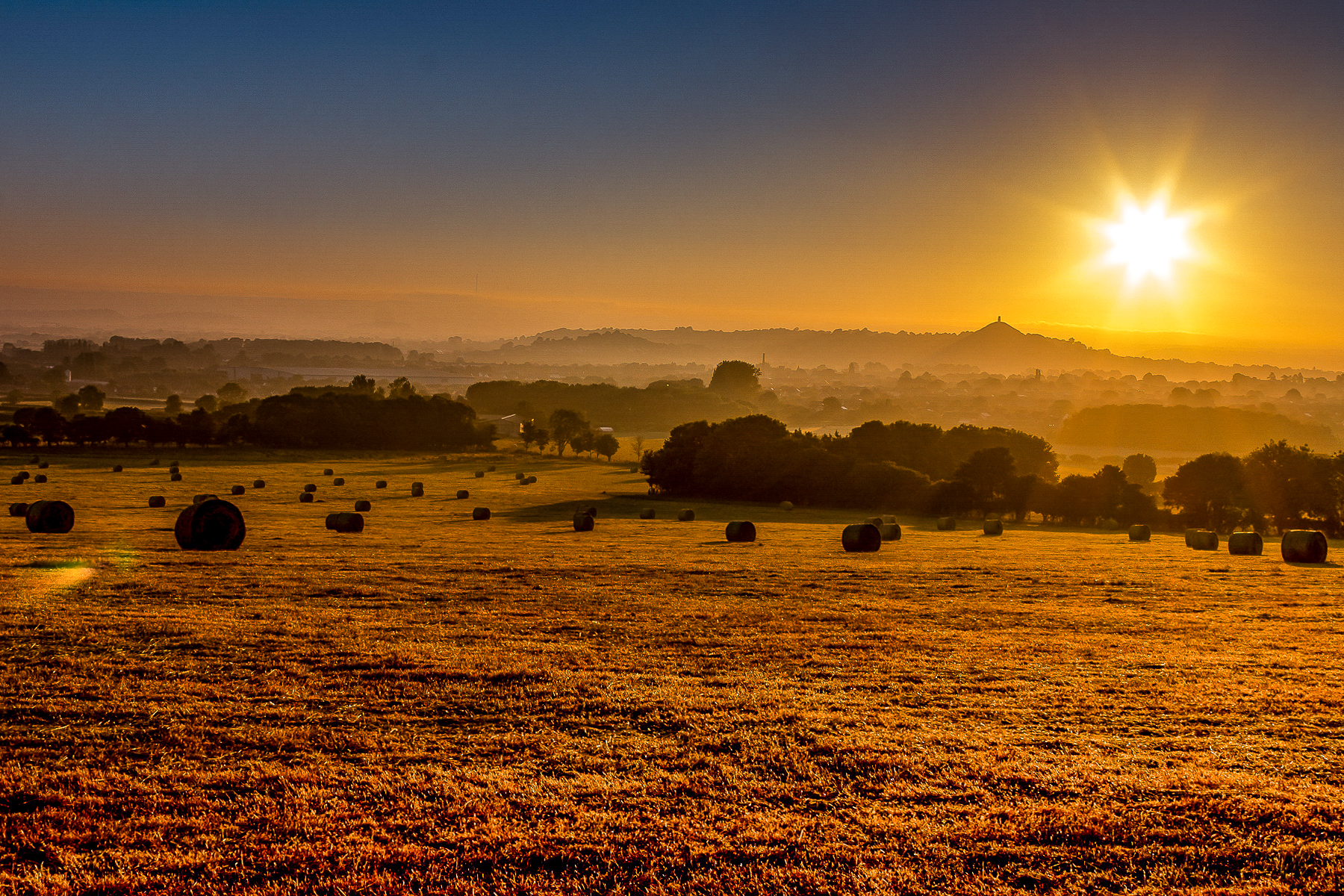 Golden light over fields with hay bales in the foreground of Glastonbury