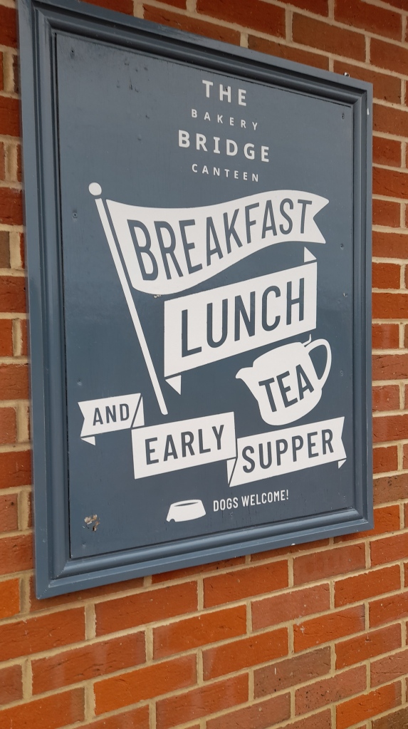 A grey sign with white writing saying breakfast, lunch, tea and early supper