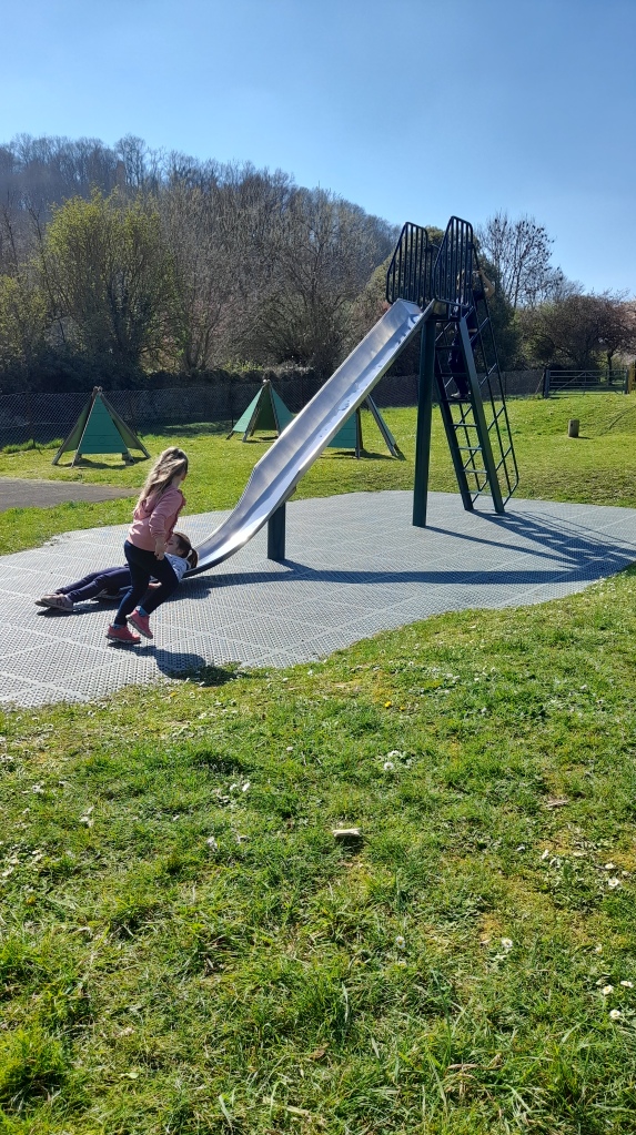 A slide in the foreground with a little girl running towards it in the background is a hill with St Michaels Tower