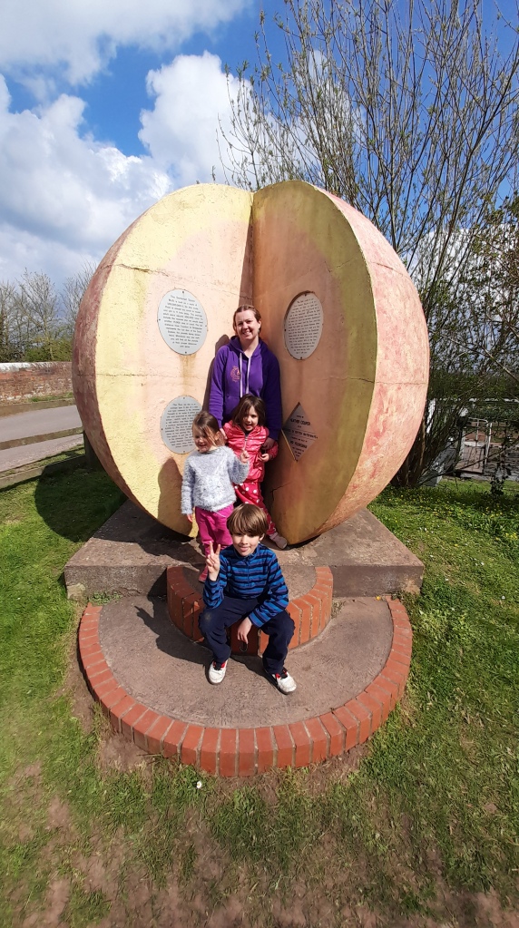 Sarah with her 3 kids standing inside a pale orange sun sculpture!