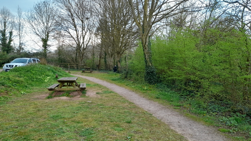 A picnic bench on a grassy bank on the edge of a car park