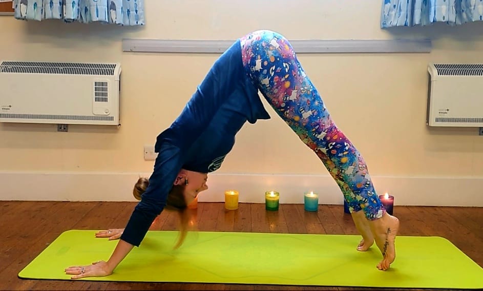 Rachael doing a Down dog yoga pose with multi coloured candles in the background