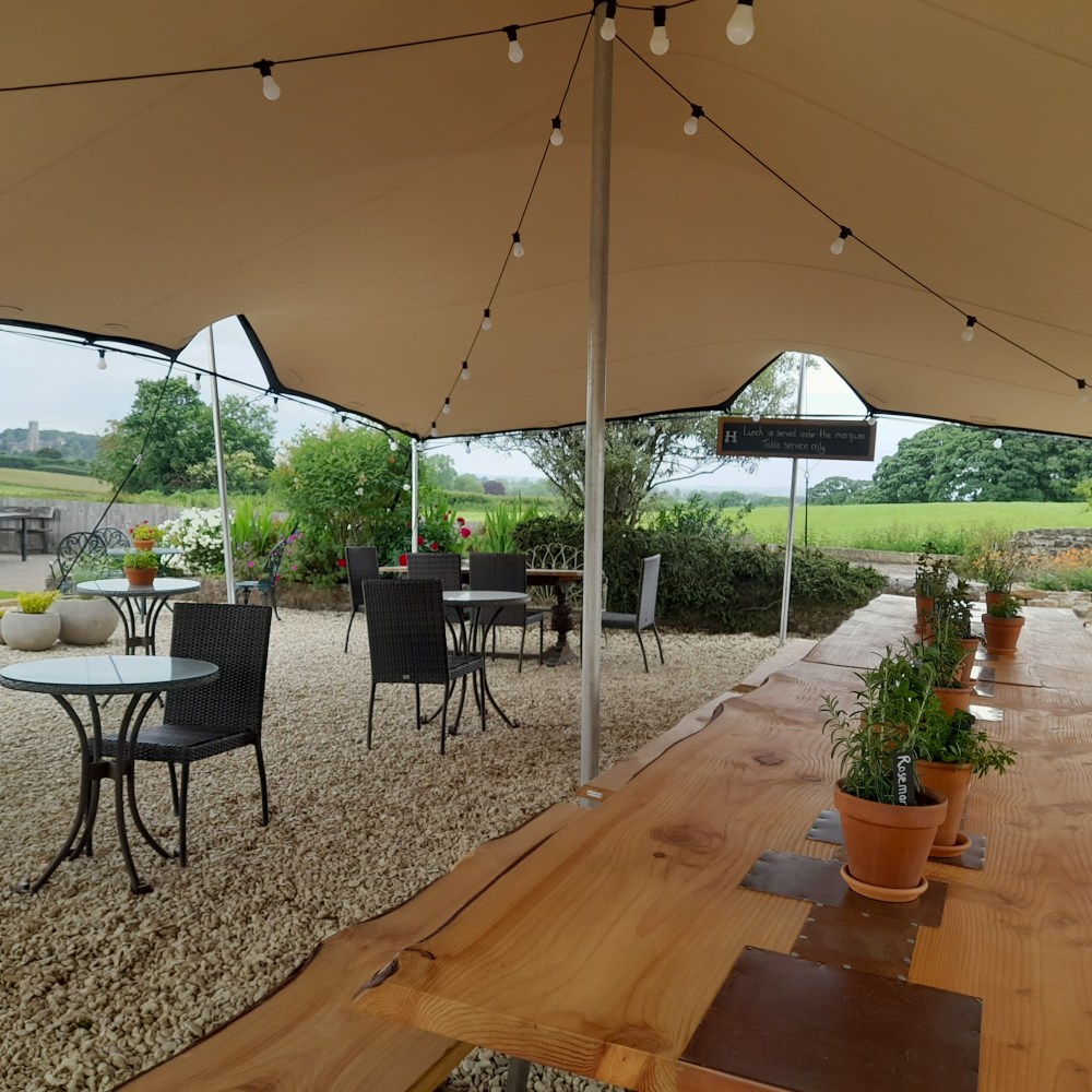 A long wooden Douglas Fir table under a canopy in green Somerset countryside