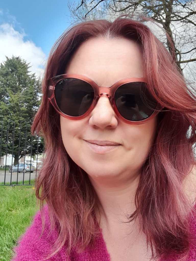 Smiling with sunglasses with long rosy coloured hair