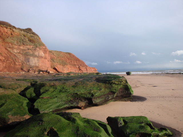 Stunning red cliffs with rocks and sandy beach in the foreground